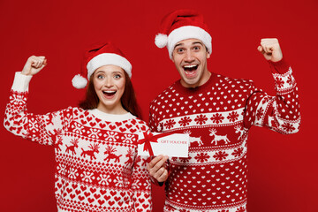 Young smiling couple friend two man woman in sweater hat hold gift certificate coupon voucher card...