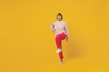 Fototapeta na wymiar Full body elderly happy fun woman 50s with bob haircut wears pink casual knitted sweater do winner gesture clench fist isolated on plain yellow background studio portrait. People lifestyle concept