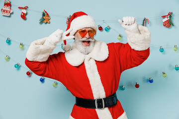 Old bearded Santa Claus man 50s wears Christmas hat red suit clothes glasses dance show v-sign isolated on plain blue background studio. Happy New Year 2022 celebration merry ho x-mas holiday concept.