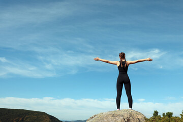 Beautiful young woman doing exercise on rock in mountains, back view