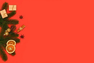 On a red background, branches of a Christmas tree and mini gifts, dry oranges.