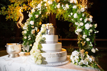 Large wedding cake arranged on a table set up in the garden in the evening with decorative flowers