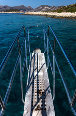A picture taken from the bow of a sailing boat and white wooden gangway with shiny metal handles...