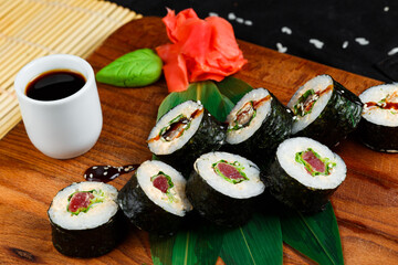 Sushi rolls with tuna and salmon on wooden board on a dark background