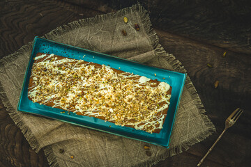 Cake with white chocolate, nuts, almonds and pistachios as a topping on wooden background, top view.