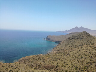 beautiful scene of a calm sea, under a blue sky with clouds and surrounded by a mountain with vegetation.