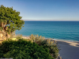 beautiful scene of a calm sea, under a blue sky with clouds and surrounded by a mountain with vegetation.