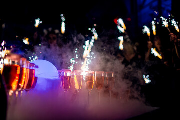 A lot of champagne flutes on banquet table with sparklers in nightclub, limited focus depth