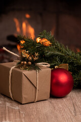gift wrapped with paper and tied with a cord decorated with a red light bulb and Christmas tree branch in the background a campfire, objects in studio, cozy space