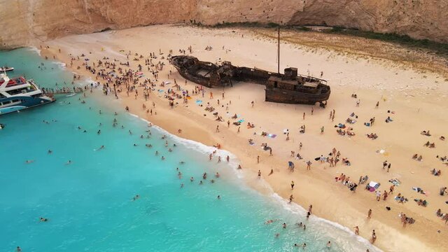 Aerial drone view of the Navagio beach on the Ionian Sea coast of Zakynthos, Greece. Moored boats and resting people, rusty ship, blue water