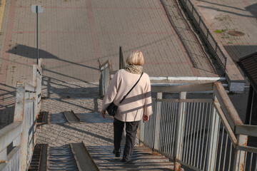 An adult woman in a light coat goes down the steps of the iron stairs to the railway platform on a sunny day
