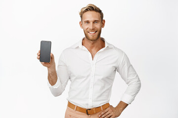 Portrait of handsome guy showing mobile phone screen and smiling, advertising app interface, website or company application, white background