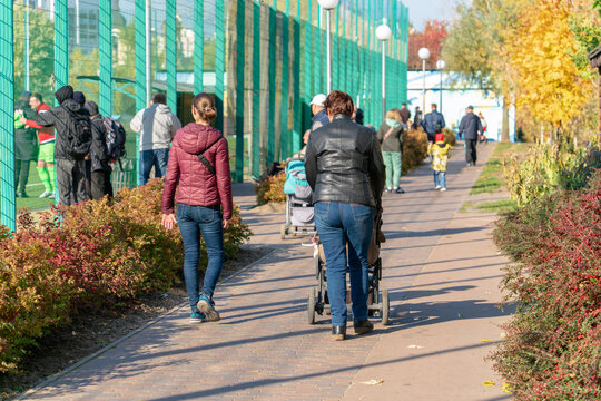 Grandma and mom with a baby carriage walk near the football stadium with the townspeople on an autumn day