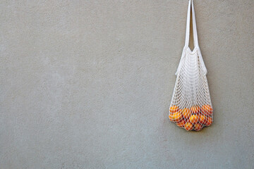 Crochet bag filled with fresh tangerines, hanging on a concrete wall.