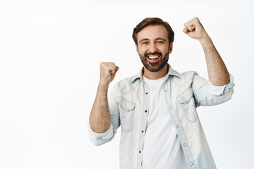 Joyful adult man rejoicing, smiling and celebrating, raising fists up and triumphing, standing over white background