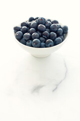 Backlit Blueberries in White Bowl on White Marble with Copy Space