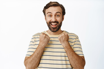 Enthusiastic happy guy winning, looking surprised and pleased, standing ecstatic against white background