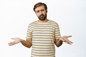 Sad and confused guy with beard, shrugging, showing empty hands sideways and furrow eyebrows upset, dont understand, standing over white background