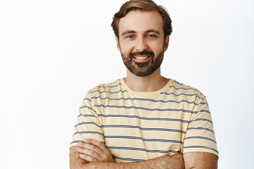 Close up portrait of handsome man with beard, smiling and looking with confident face, cross arms like professional, standing over white background