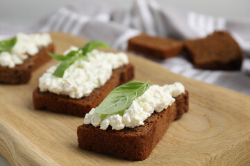 Fototapeta na wymiar Bread with cottage cheese and basil on wooden board, closeup
