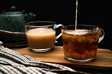 Healthy tea poured into transparent cup. Teapot, lemon, ginger, cardamom, heather bunch and glass jar of daisy teabags