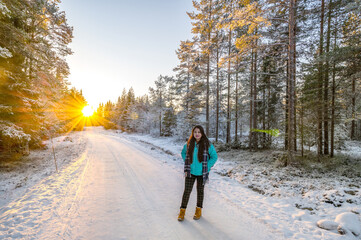 A calm tranquil view of the snow covered trees in the snowdrifts and beautiful sunset. A beautiful woman in coloured jacket walking through the Magical winter forest.