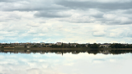 A small village on the shore of a lake on a cloudy morning before the rain. Houses, trees and clouds are beautifully reflected in the water. Copy space.