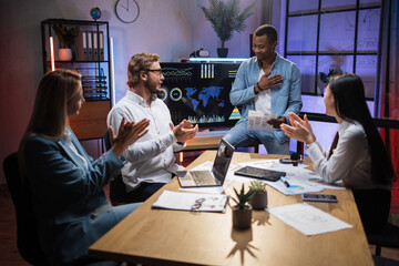 Multi ethnic company workers applauding to his african colleague during working meeting at modern office. Four people gathering at room for planning business strategy.