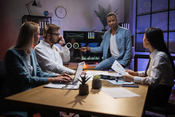 Multiracial business people having briefing about financial situation at company. African man pointing on monitor with various graphs and charts. Cooperation and brainstorming concept.