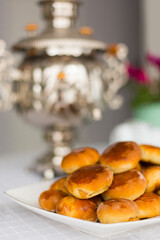 Russian traditional teaparty with samovar and pies or pirozhki with apple jam on white platter on white tablecloth 