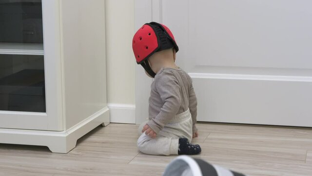 Cute baby boy wearing soft safety helmet discovering new things at home, 7 month old infant on the floor playing, learning to walk, craw sit and stand. High quality 4k footage