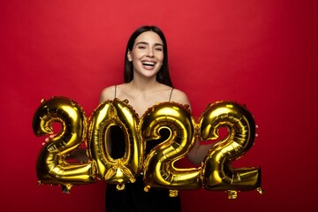 A young cheerful woman in a black dress holds the numbers 2022