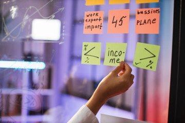 Close up of female hand putting paper stickers on transparent board. Flip chart with financial strategy for company development. Business meeting concept.
