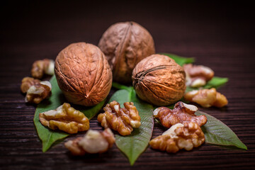 Fototapeta premium Walnuts - shelled and kernels with green walnut tree leaves isolated on dark background