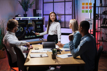 Group of competent diverse economists discussing business ideas while gathering at office room. Asian woman standing near bid monitor with various graphs and charts.