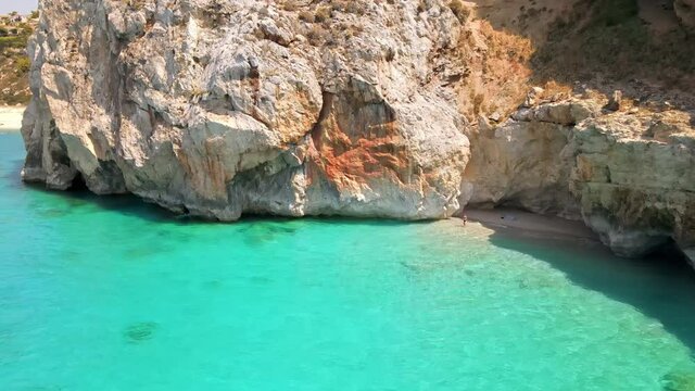 Aerial drone view of the Ionian Sea coast of Zakynthos, Greece. Rocky cliff, vegetation, small beach with a woman, blue water