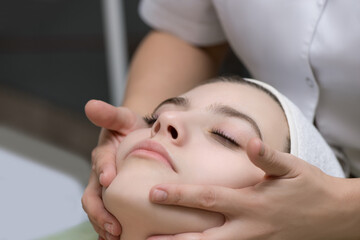 Fototapeta na wymiar Face massage. Close-up of young woman getting spa massage treatment at beauty spa salon. Spa skin and body care. Facial beauty treatment. Selective focus.