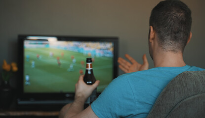 Man with bottle of beer watching football on TV.