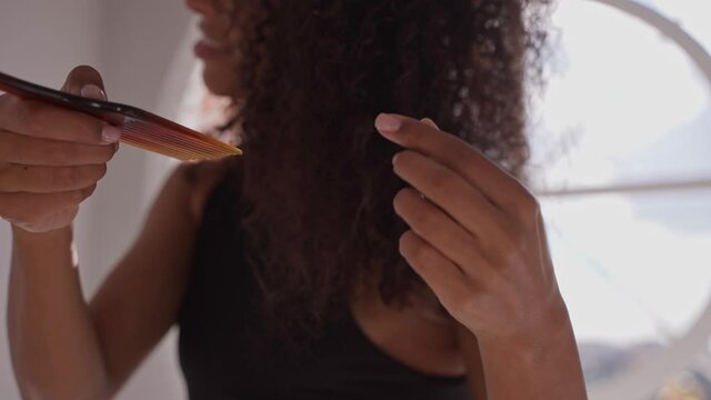 Happy black woman combing her afro hair after taking a bath in bright white room. Taking hair care of afro standing in bright white bathroom with round window. High quality 4k footage