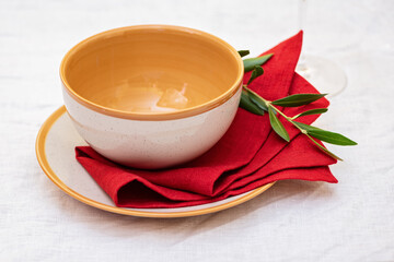 Plate with a spoon, red linen napkin and olive branch on a table with table cloth