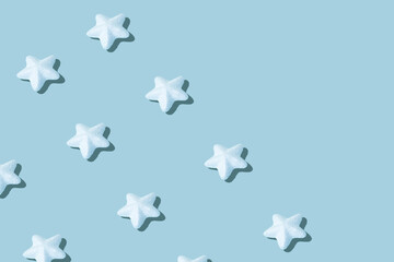Christmas creative pattern made of sparkling white stars against ice blue background. Winter holidays and New Year concept.