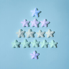 Christmas tree made of sparkling stars in vibrant neon colours against icy blue background. Creative festive and New Year layout.