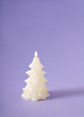 Christmas tree shiny candle with flame against pastel purple background. Winter holidays and New Year idea.