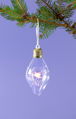 Lightbulb with sparkler fireworks in it hanging from Christmas natural fir branch. Pastel purple background. Winter holidays and New Year idea.
