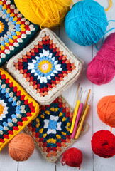 Handmade crocheting granny square, a hook and yarn balls.