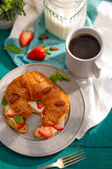 Stylish composition. Table served for breakfast for one person. Croissant, fresh strawberries, almonds, mint leaves and a cup of black coffee. Restaurant, hotel, home comfort.