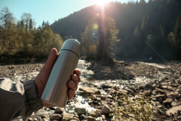 Man holding thermos in mountains, closeup. Space for text