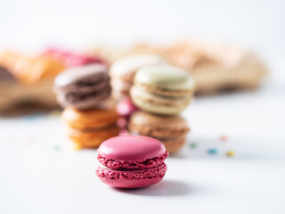 Multicolored macaroon cookies on the white background. Pink, orange, and coffee macaroon in the foreground