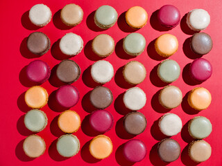 The pattern of multicolored macaroon cookies. Pink, green, coffee, and red on red background
