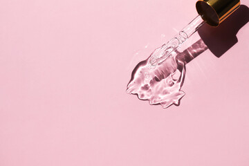 A drop of hyaluronic acid and a glass pipette on a pink background. Top view, place for text.